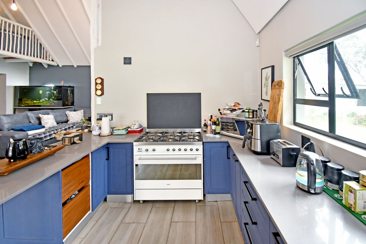 Modern kitchen featuring blue cabinetry, stone countertops, a gas cooktop with freestanding oven, and tiled flooring, with an open-plan layout to the living area.