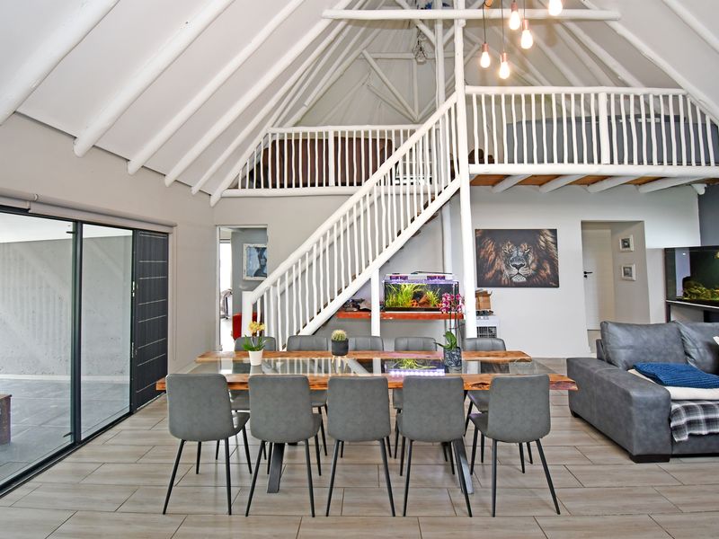 Spacious open-plan living and dining area featuring a double-volume ceiling with exposed rafters, a mezzanine level, and large sliding doors leading to the patio.