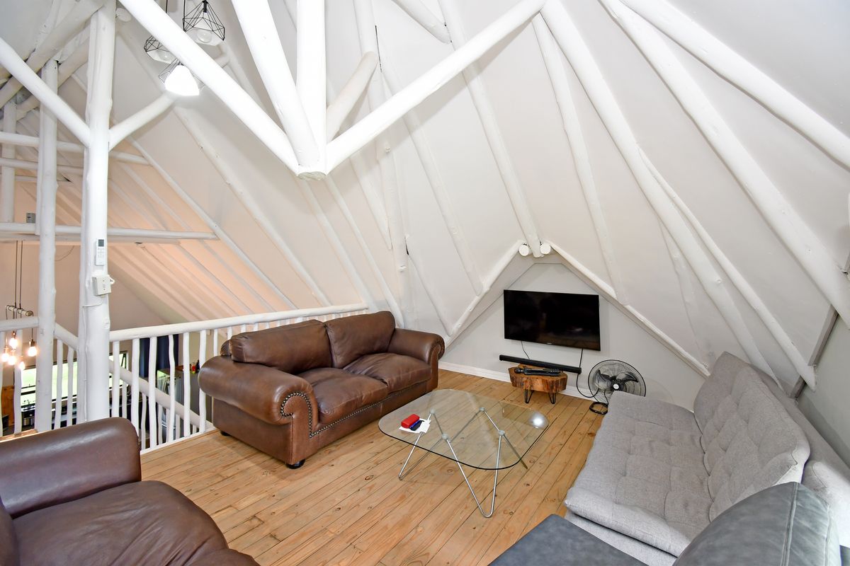 A cozy loft-style living area featuring exposed white timber roof trusses, warm timber flooring, and a mezzanine overlook.