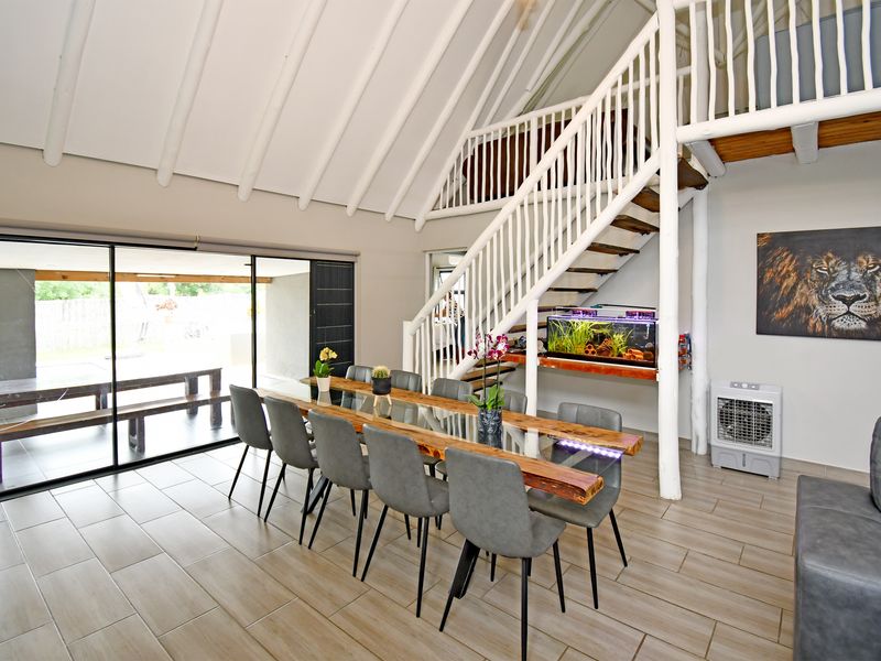 Spacious open-plan dining area featuring a vaulted ceiling with exposed rafters, a mezzanine level, and large sliding glass doors leading to the patio.