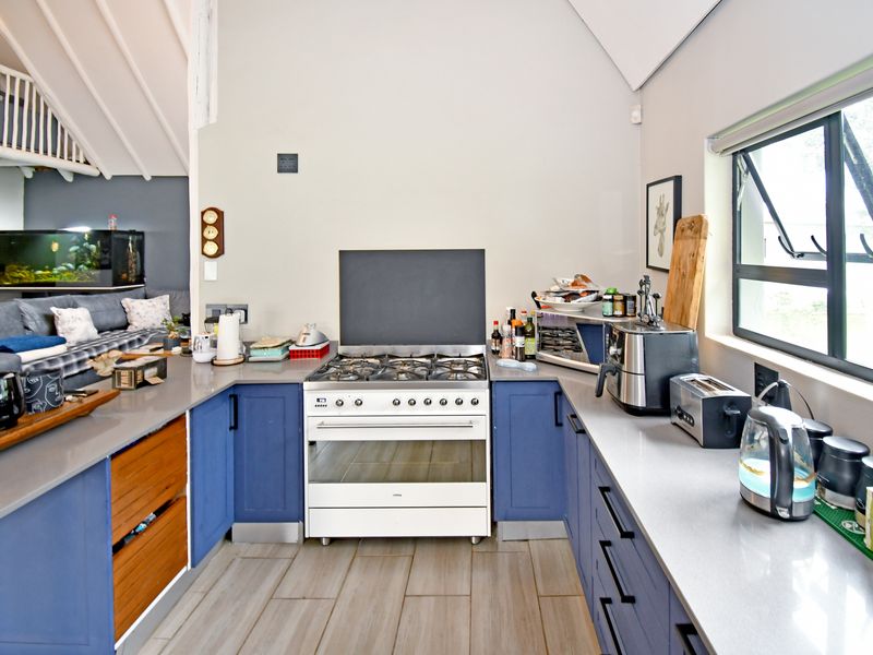 Modern kitchen featuring blue cabinetry, stone countertops, a gas cooktop with freestanding oven, and tiled flooring, with an open-plan layout to the living area.