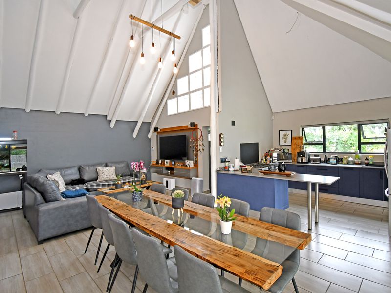 Spacious open-plan living area featuring a vaulted ceiling with exposed rafters, a modern kitchen with island, and large windows providing ample natural light.