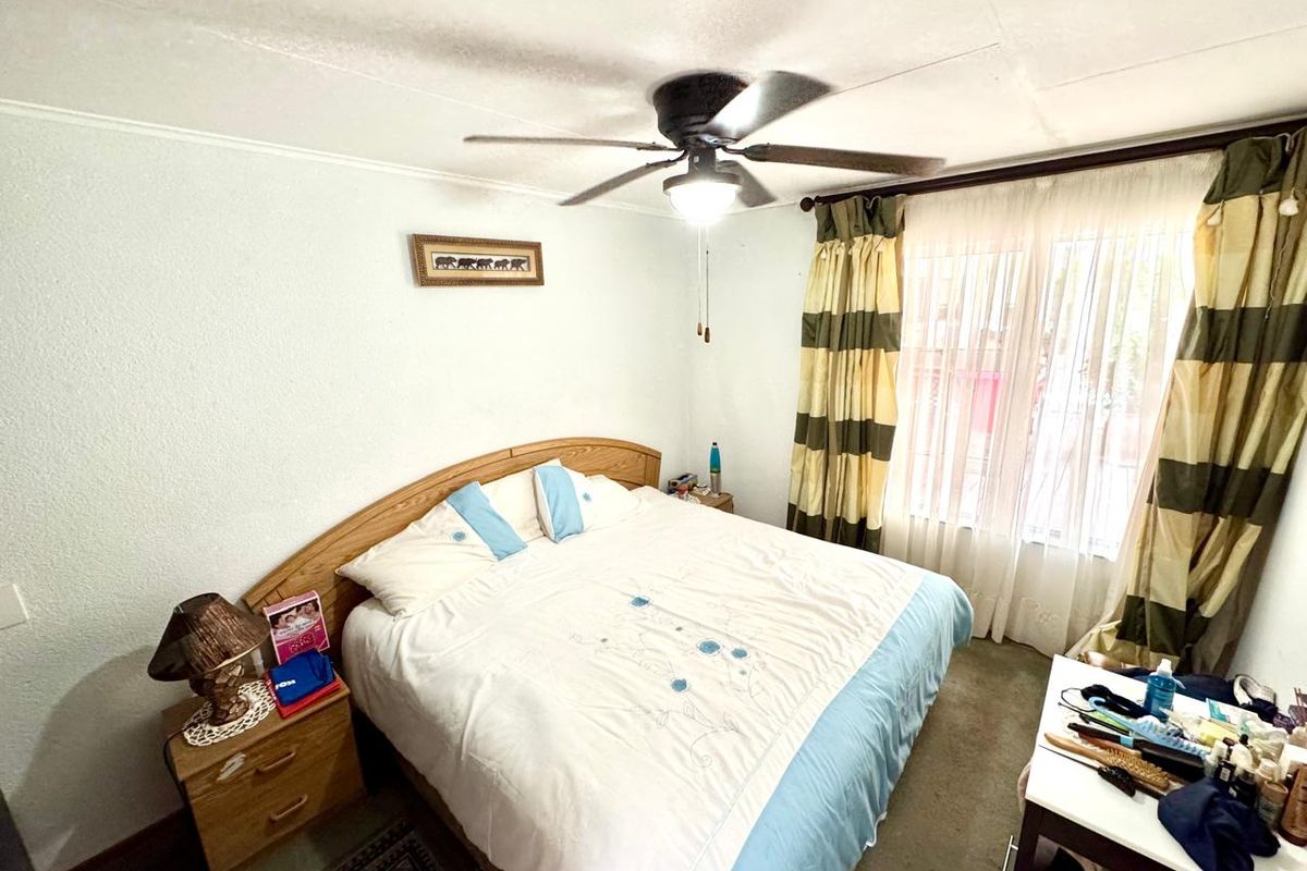 A functional bedroom featuring a ceiling fan and natural light through a window with curtain fixtures.
