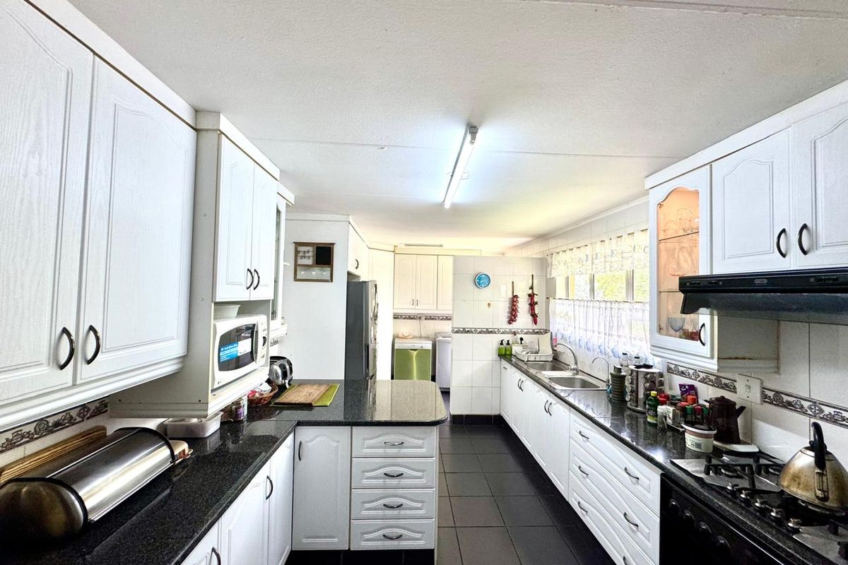 A functional galley-style kitchen featuring white cabinetry, dark granite countertops, a built-in gas hob, and an integrated extractor fan.