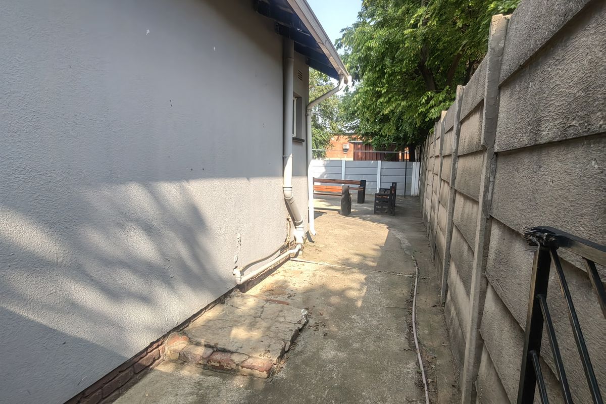 A narrow rear exterior walkway featuring concrete paving, a plastered building facade, and a precast concrete boundary wall.