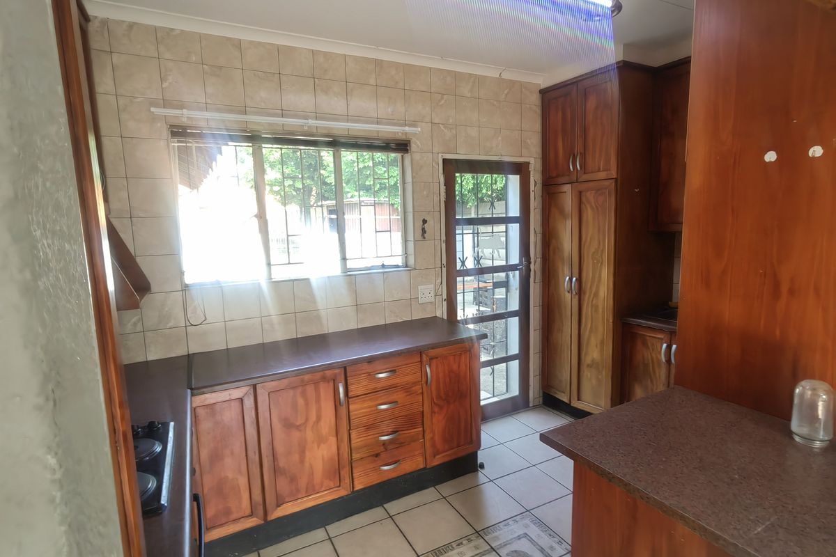 A functional kitchen featuring wooden cabinetry, laminate countertops, tiled flooring, and a built-in hob, with direct access to the exterior.