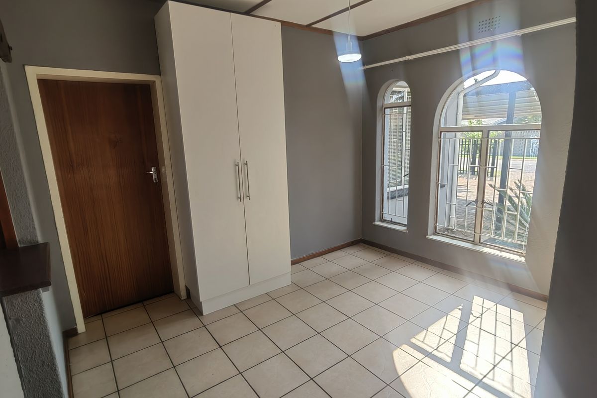 A bright, empty bedroom featuring tiled flooring, a built-in wardrobe, and arched windows with security bars.