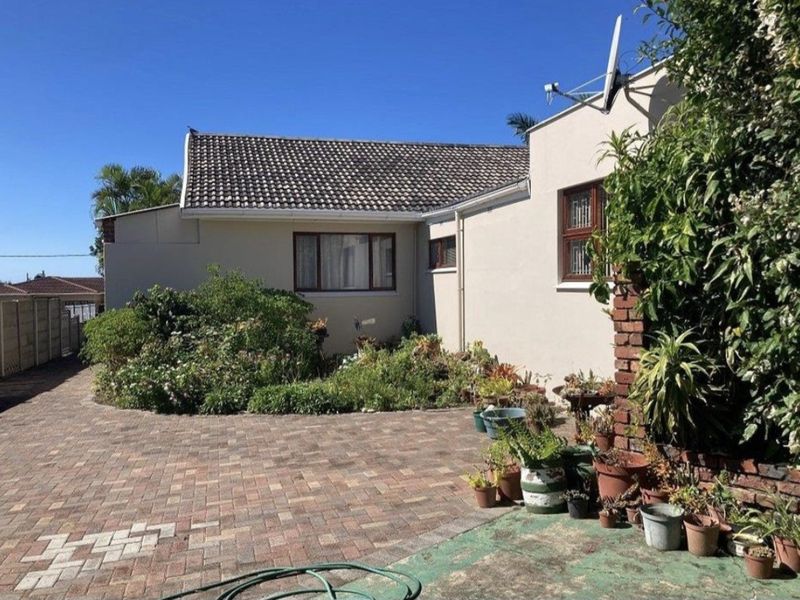 Front exterior view of the house featuring a paved driveway, tiled roof, and established garden beds.