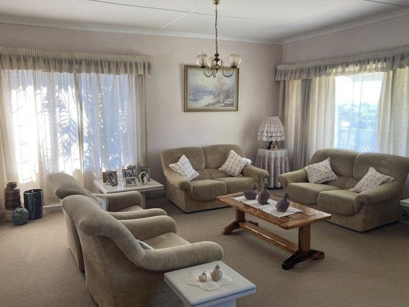 A spacious living room featuring neutral carpeting, coved ceilings, and large windows with curtain rails, offering a comfortable and traditional living space.