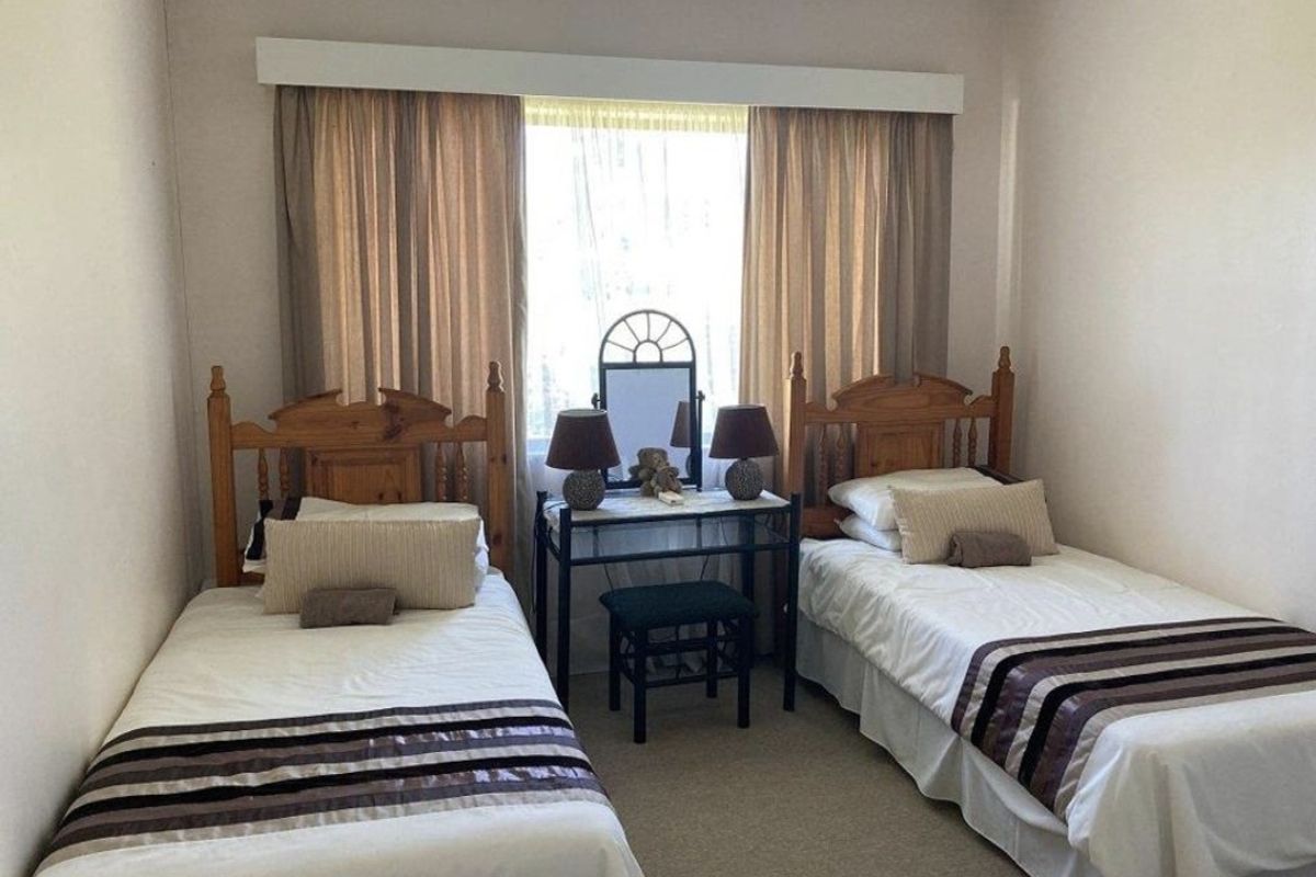 A functional bedroom featuring neutral wall tones, carpeted flooring, and a window dressed with a curtain pelmet.
