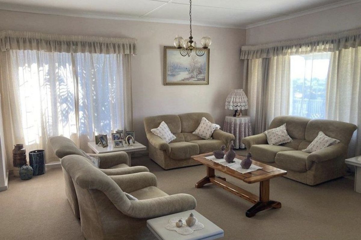 A spacious living room featuring neutral carpeting, coved ceilings, and large windows with curtain rails, offering a comfortable and traditional living space.