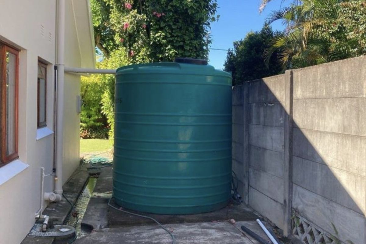 Side exterior area featuring a large green water storage tank, concrete paving, and a boundary wall.