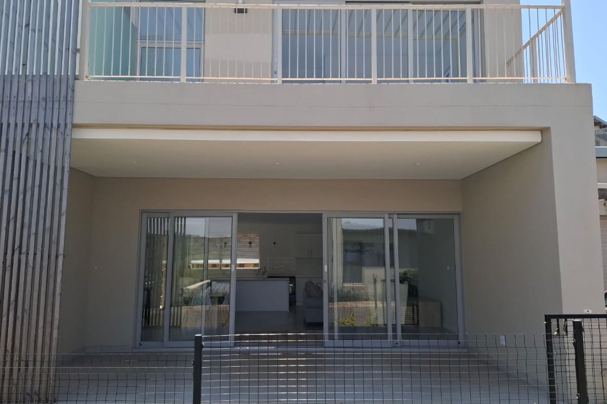 Rear elevation of a modern two-story house featuring a ground-floor patio with sliding glass doors and an upper-level balcony with a metal balustrade.
