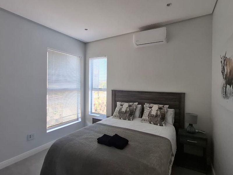 A well-maintained bedroom featuring neutral walls, recessed downlighting, venetian blinds, and a wall-mounted split-system air conditioning unit.