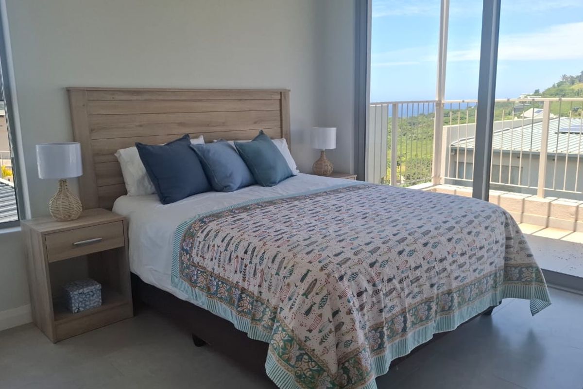 A bright bedroom featuring large sliding glass doors that open onto a balcony with scenic views, complemented by modern tiled flooring.