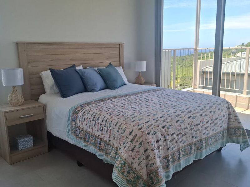 A bright bedroom featuring large sliding glass doors that open onto a balcony with scenic views, complemented by modern tiled flooring.