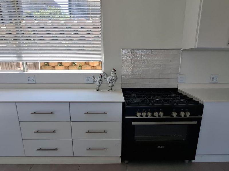 A clean, modern kitchen featuring white cabinetry, stone countertops, a subway tile backsplash, and a black gas stove with oven.