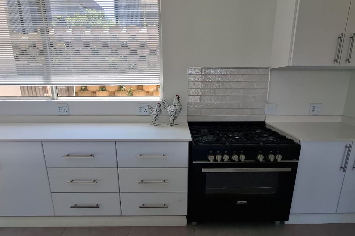 A clean, modern kitchen featuring white cabinetry, stone countertops, a subway tile backsplash, and a black gas stove with oven.