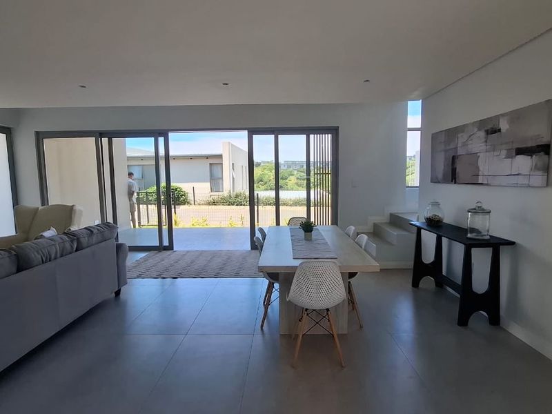 Spacious open-plan living and dining area featuring large sliding glass doors that open onto an outdoor patio, with modern tiled flooring and recessed lighting.