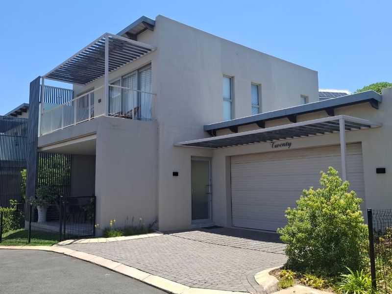 Modern double-story residential property featuring a paved driveway, integrated double garage, and an upper-level balcony with metal pergola detailing.