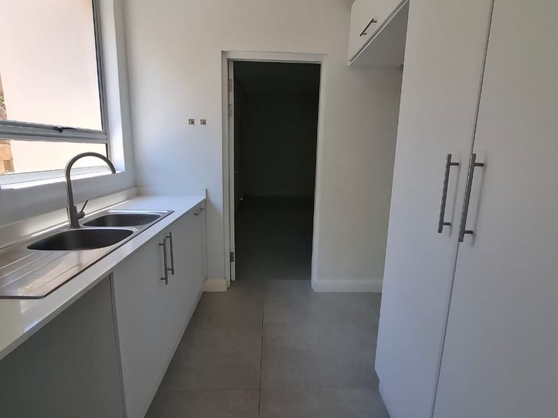 A clean and functional scullery area featuring modern white cabinetry, a double bowl sink with mixer tap, and neutral tiled flooring.