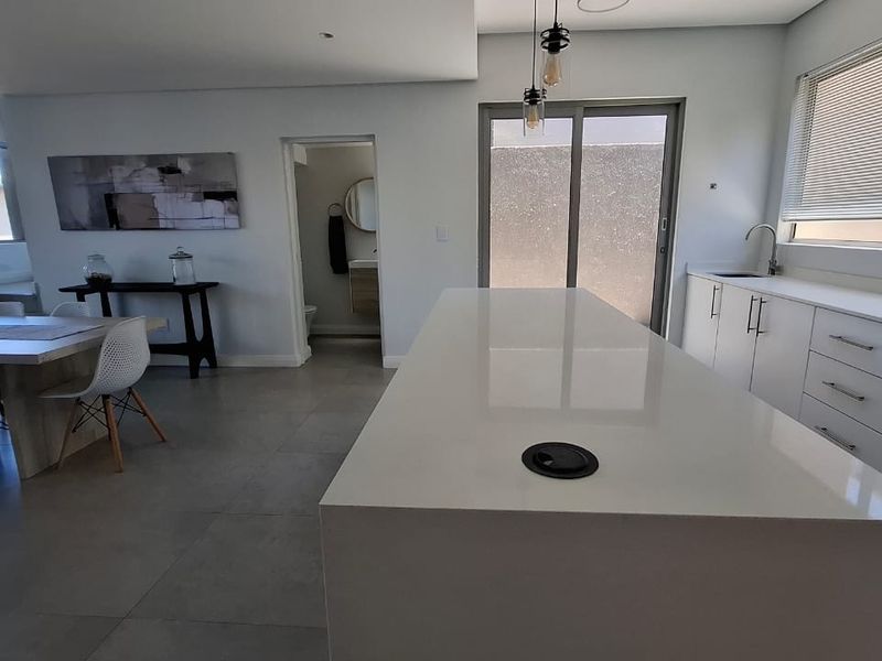 Modern open-plan kitchen and dining area featuring a large central island with quartz countertops, sleek cabinetry, and direct access to the outdoor space.