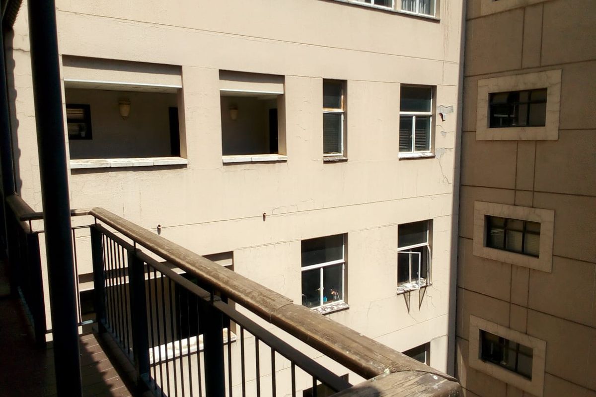View from a balcony overlooking the rear facade of an apartment building, showing visible wear to the exterior plaster and paintwork.