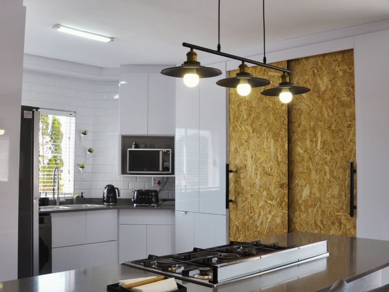 Modern kitchen featuring white cabinetry, subway tile backsplash, stone countertops with an integrated gas hob, and unique sliding OSB panel doors.