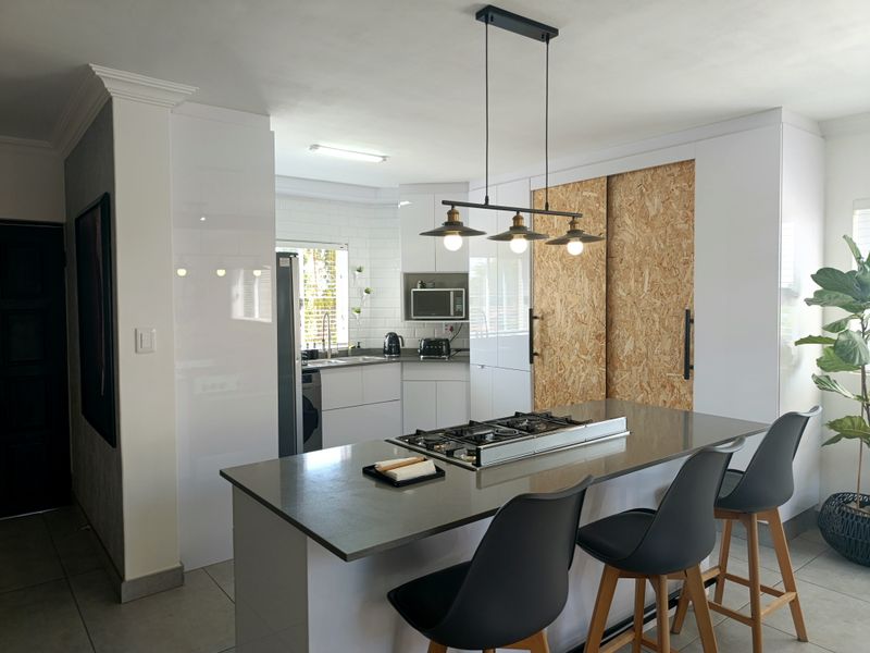 Modern kitchen featuring a central island with a gas cooktop, sleek white cabinetry, subway tile backsplash, and contemporary pendant lighting.
