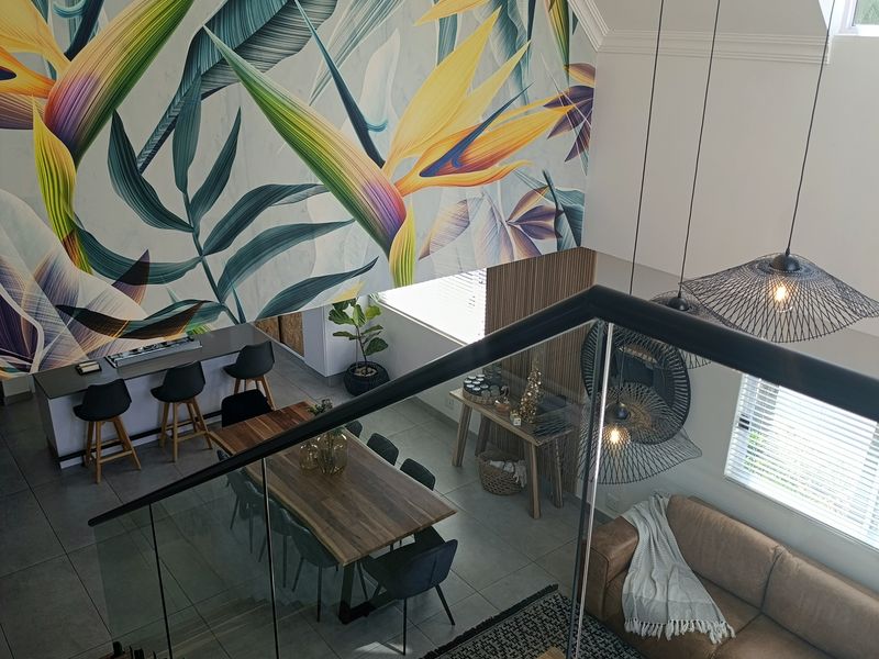 Spacious open-plan living and dining area featuring high ceilings, a striking feature wall, modern tiled flooring, and a glass-railed staircase.