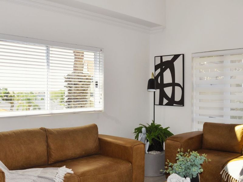 A bright living room featuring high ceilings, crown molding, and dual-style window blinds providing natural light and exterior views.