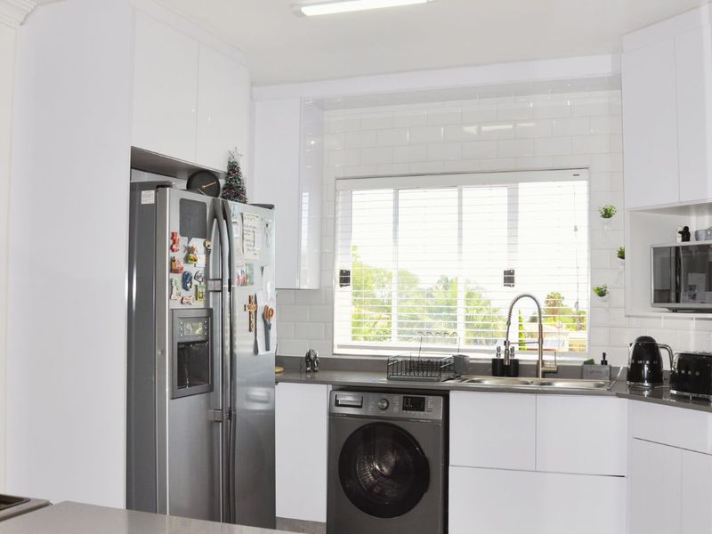 Modern kitchen featuring white cabinetry, subway tile backsplash, stone countertops, and integrated laundry facilities under a bright window.