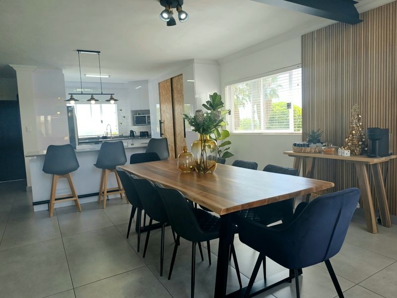 Modern open-plan living and dining area featuring a kitchen island, contemporary cabinetry, and stylish slatted wood wall paneling with large format floor tiles.