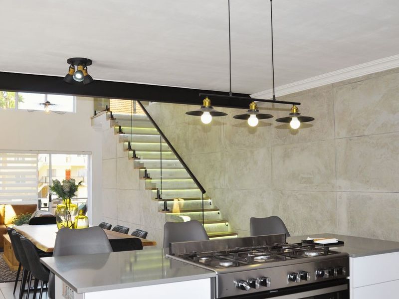 Modern open-plan living area featuring a sleek kitchen island with gas cooktop, concrete feature wall, and a contemporary staircase with integrated lighting.