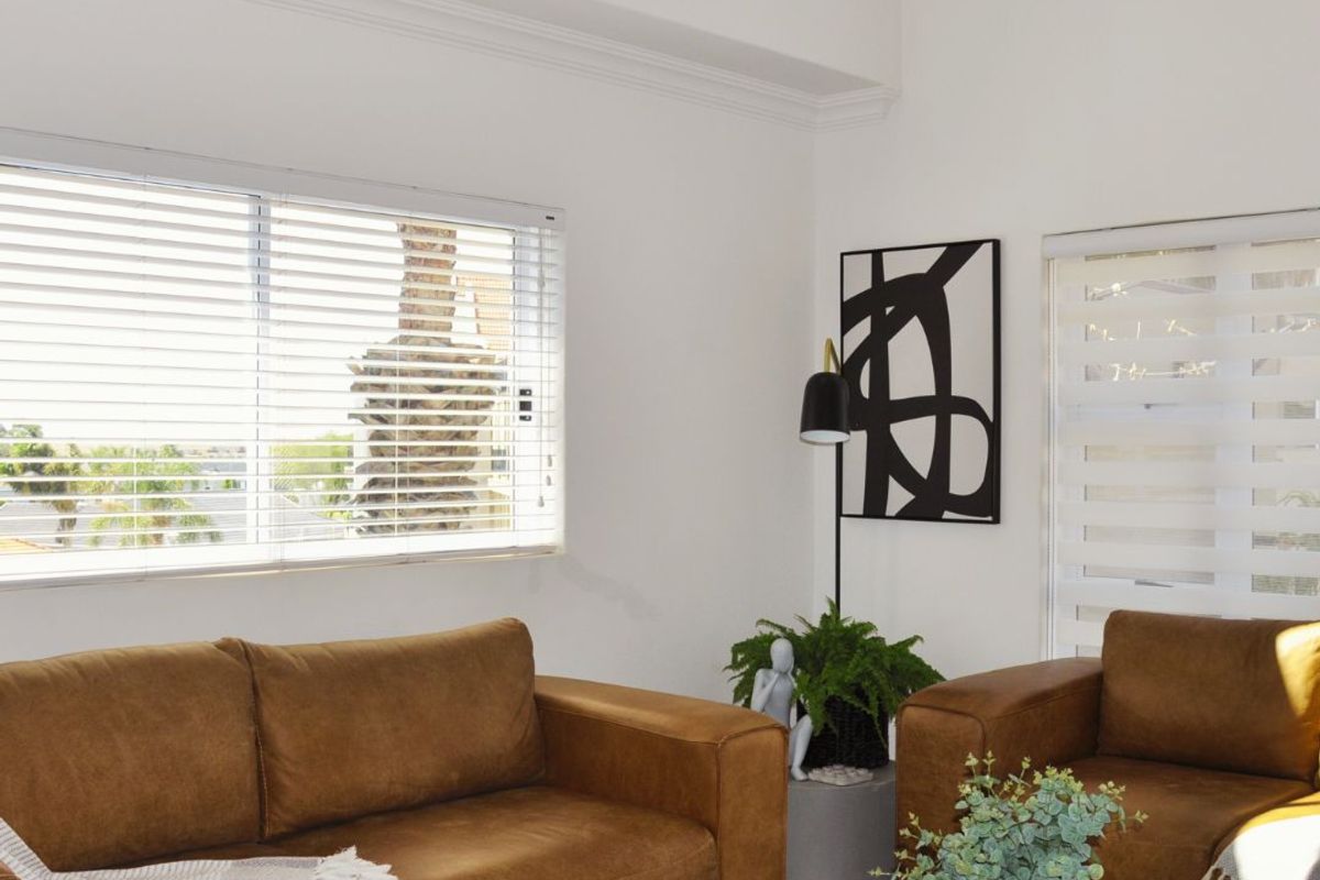 A bright living room featuring high ceilings, crown molding, and dual-style window blinds providing natural light and exterior views.