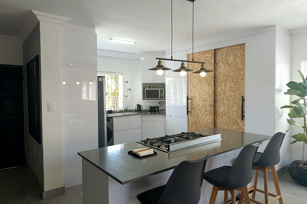 Modern kitchen featuring a central island with a gas cooktop, sleek white cabinetry, subway tile backsplash, and contemporary pendant lighting.