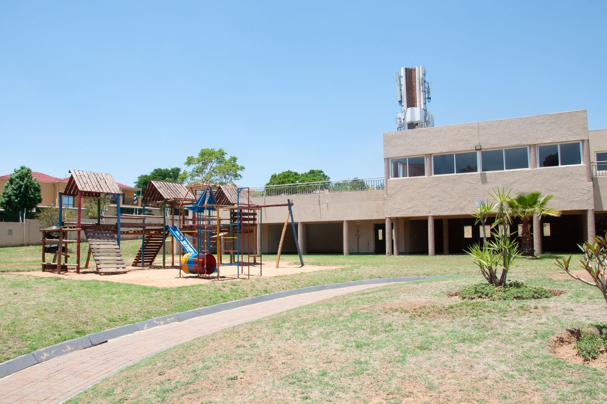 Rear exterior view of the apartment complex featuring a communal lawn, playground equipment, and a covered patio area.