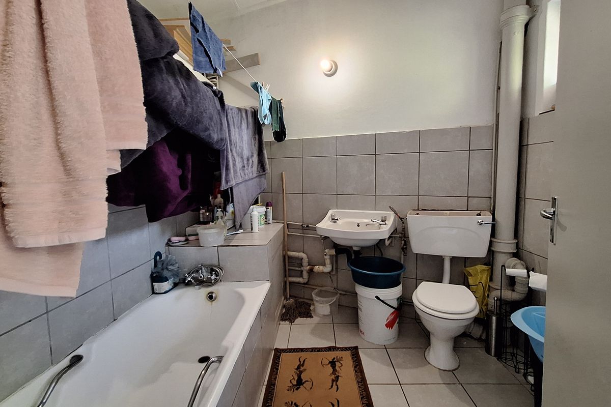 A functional bathroom featuring a bathtub, wall-mounted basin, and toilet with tiled finishes and exposed plumbing elements.