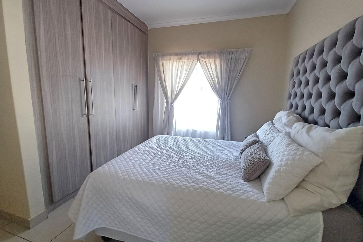 A well-maintained bedroom featuring neutral tiled flooring, coved ceilings, and extensive built-in wooden cupboards providing ample storage space.