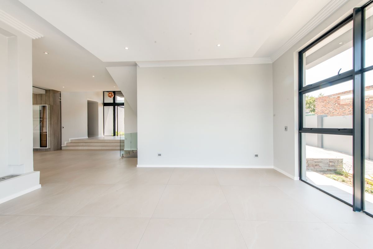 A bright, spacious, and modern open-plan living area featuring large format floor tiles, recessed lighting, and expansive black-framed windows overlooking the exterior.