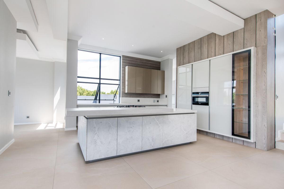 Modern, high-end kitchen featuring a large marble-topped island, integrated cabinetry, built-in oven, and sleek contemporary finishes in an open-plan layout.