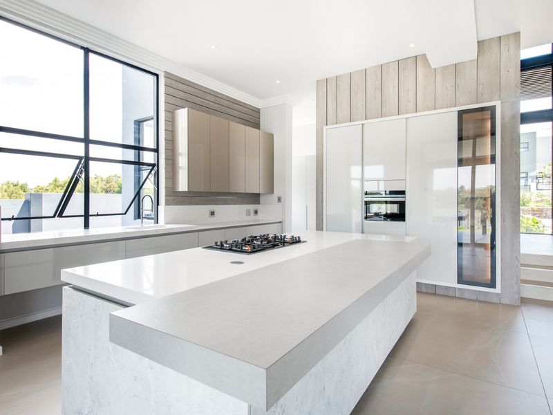 Modern, high-end kitchen featuring a large central island with stone countertops, integrated appliances, sleek cabinetry, and expansive windows providing ample natural light.
