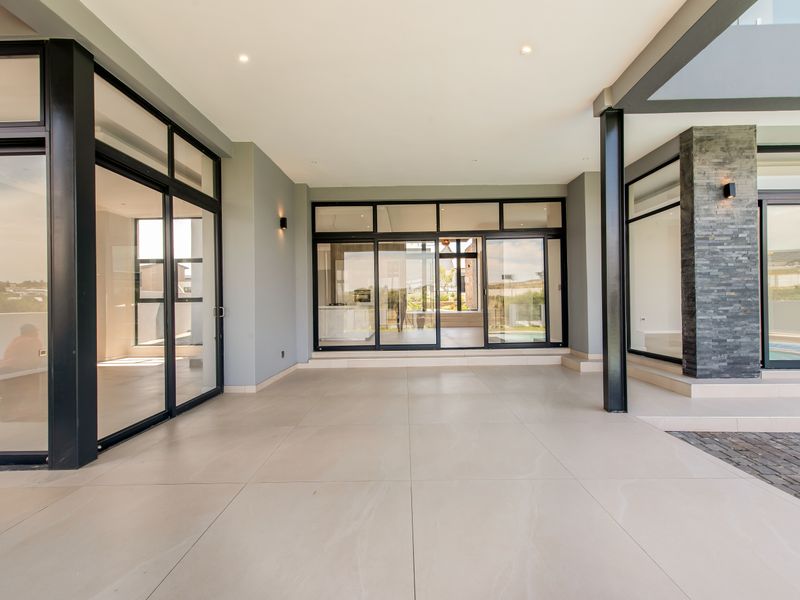 A spacious, modern covered patio featuring large format floor tiles, black aluminium sliding doors, and a stylish stone-clad feature pillar.