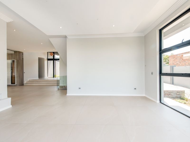 A bright, spacious, and modern open-plan living area featuring large format floor tiles, recessed lighting, and expansive black-framed windows overlooking the exterior.