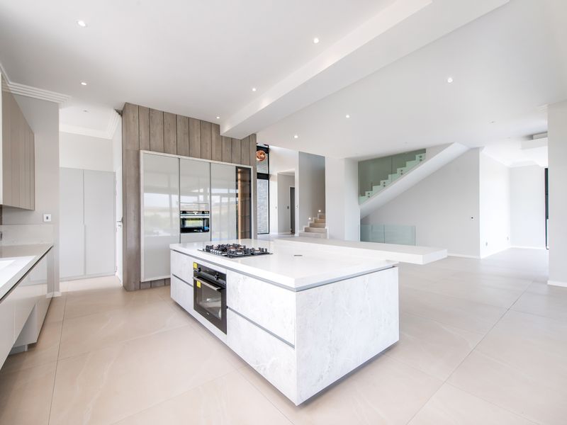 Modern open-plan kitchen featuring a large stone-topped island with integrated gas cooktop and oven, complemented by sleek cabinetry and high-end finishes.