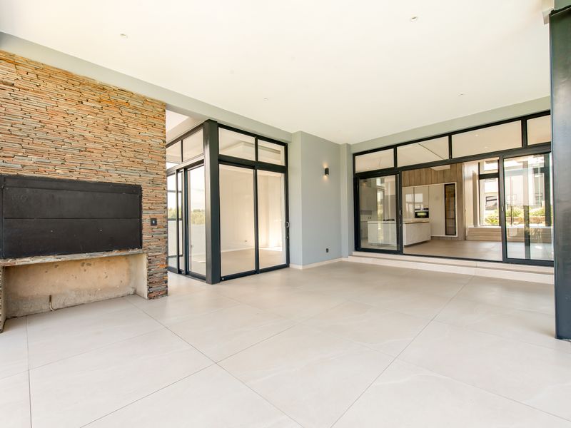 Spacious covered patio featuring a stone-clad feature wall with a built-in braai, large format floor tiles, and expansive aluminium sliding doors leading indoors.