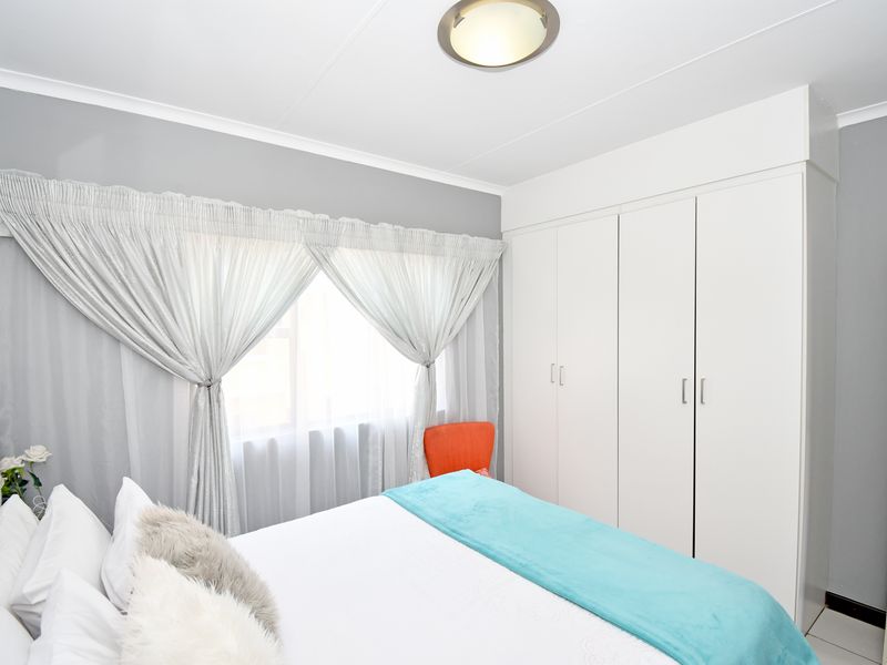 A well-maintained bedroom featuring neutral grey walls, white built-in cupboards, and a ceiling light fixture.
