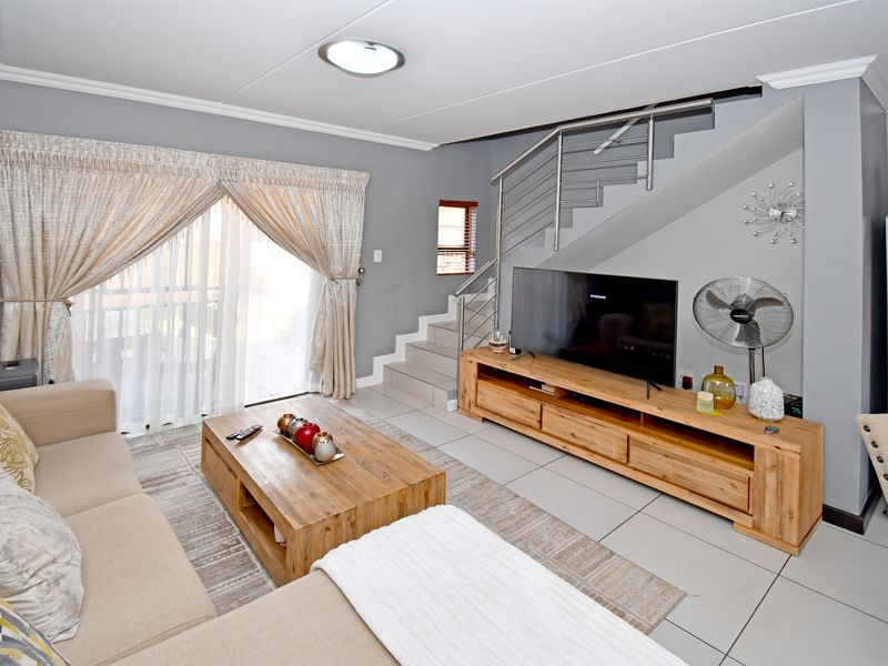 A well-maintained living room featuring tiled flooring, a modern stainless steel staircase railing, and a sliding glass door providing access to the exterior.