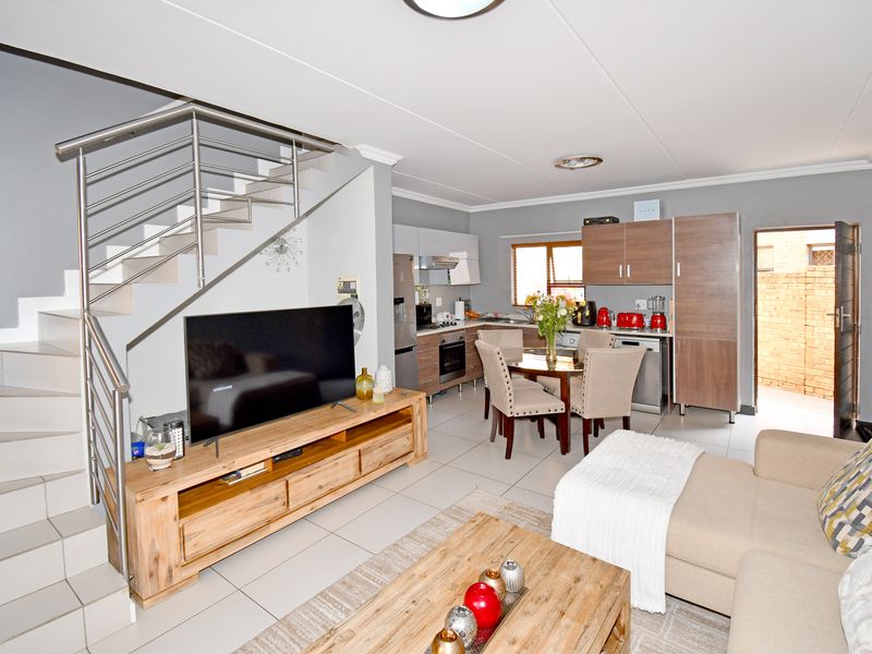 Open-plan living and kitchen area featuring a modern staircase with stainless steel balustrade, tiled flooring, and functional built-in kitchen cabinetry.