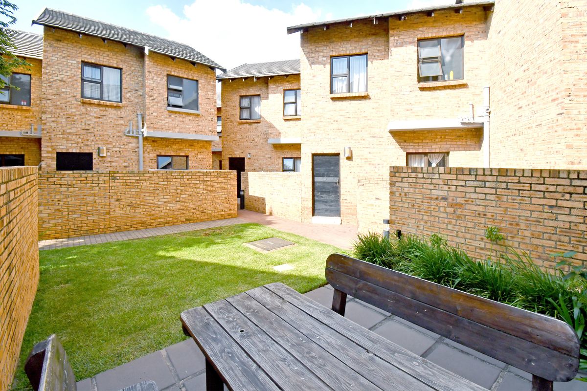 A private rear courtyard featuring a paved patio area, small lawn, and face brick exterior walls of the apartment complex.